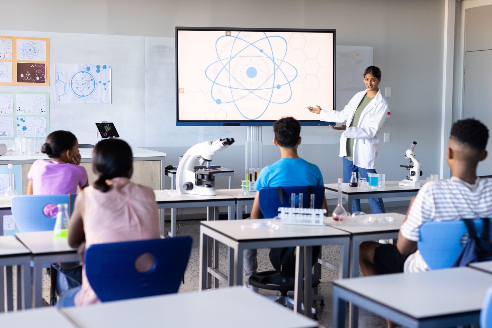 In school, Indian female teacher presenting scientific diagram on screen to students in classroom